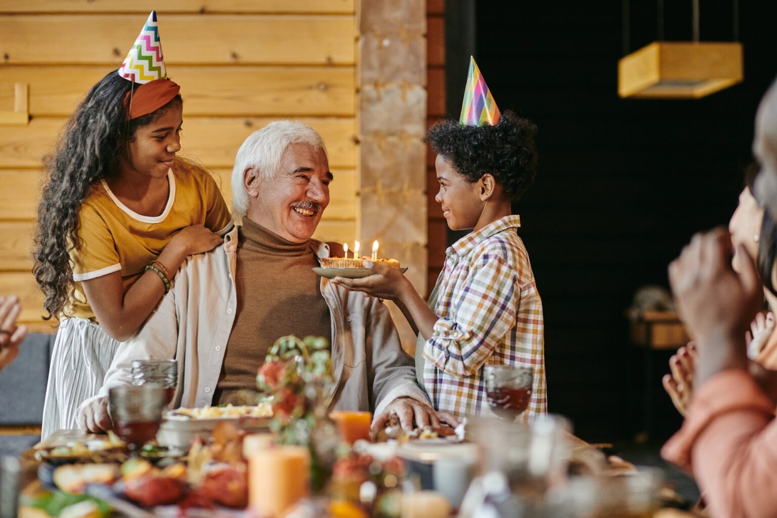 Happy aged man looking at his interracial grandson with birthday cake